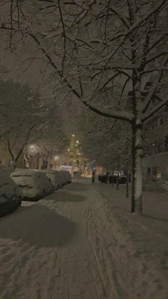 a snowy street with cars parked on the side and people walking down the sidewalk at night