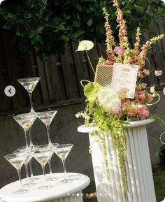 a table topped with wine glasses filled with flowers next to a tall white planter