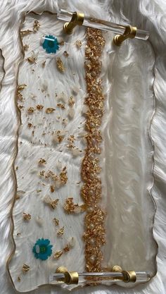 a glass tray with gold and blue decorations on it, sitting on a white sheet