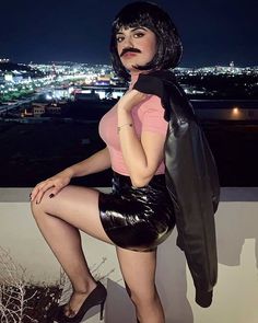 a woman in latex is posing on a ledge with a jacket over her shoulder