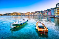 two boats in the water next to each other near some buildings and hills on the shore