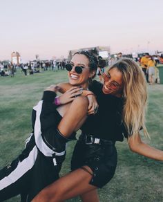 two women hugging each other in the middle of a grassy field at an outdoor music festival