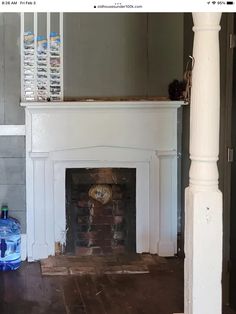 a fireplace with a clock on the mantle and water bottles sitting next to it in an empty room