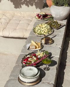 an outdoor table with plates and bowls of food on it next to a potted plant