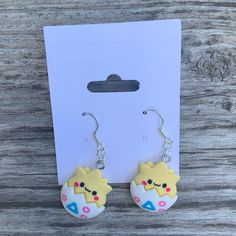 a pair of earrings with cartoon characters on them sitting in front of a white card