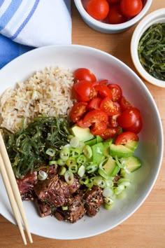 a white bowl filled with meat and vegetables next to chopsticks on a wooden table