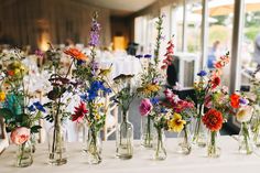 several vases filled with different types of flowers on a table at a wedding reception