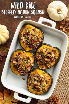 four stuffed acorn squash in a white dish on a table with autumn leaves and pumpkins