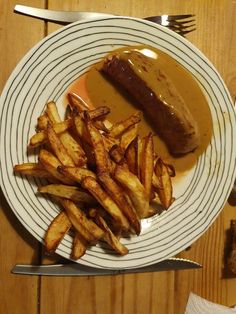 a white plate topped with french fries and a hot dog covered in gravy