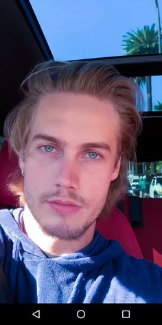 a man sitting in the back seat of a car with blue eyes and long hair