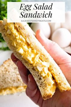 an egg salad sandwich is being held by someone's hand with eggs in the background