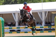 a man riding on the back of a brown horse over an obstacle