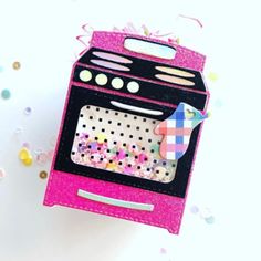 a pink box with an oven on it and confetti scattered around the edges