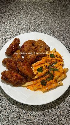 a white plate topped with chicken wings and cheesy pasta on top of a counter