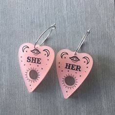 Be your most authentic, spooky you and share your pronouns with the world with these pronoun planchette earrings. If you would like to mix and match, choose the custom option and let us know what pronouns you want in the notes section of your order. Have sensitive ears? No problem, we've got you covered with options of Sterling Silver posts, Hypoallergenic Stainless Steel Posts, or Stainless Steel Hoops. Planchette measures 1.5in long and 1in wide. Handmade Edgy Plug Earrings As Gift, Handmade Edgy Plug Earrings For Gift, Edgy Nickel-free Earrings For Gift, Handmade Edgy Earrings For Festivals, Edgy Nickel-free Plug Earrings As Gift, Nickel Free Edgy Plug Earrings As Gift, Edgy Hypoallergenic Earrings For Gifts, Edgy Pink Jewelry For Gifts, Edgy Pink Jewelry For Gift