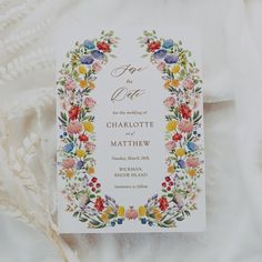 a wedding card with colorful flowers and leaves on it, sitting on a white cloth