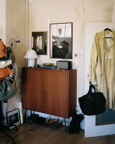 a wooden cabinet sitting in front of a wall with pictures on it and a coat rack