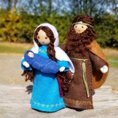 two dolls are standing next to each other on a wooden table in front of some trees