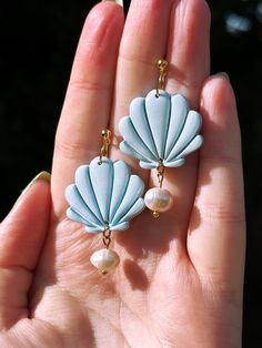 a hand holding two earrings with pearls and shell shapes on them, both in blue