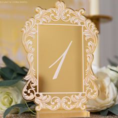 a gold and white wedding table number with flowers in the backgroung behind it