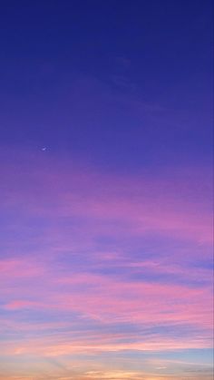 the sky is pink and purple as the sun sets in the distance with an airplane flying overhead