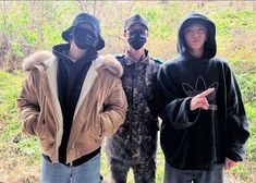 three young men standing next to each other in the woods wearing masks and hoods