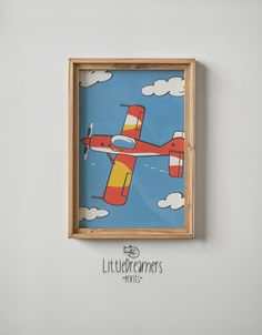 a small wooden frame hanging on the wall with a painting of an airplane flying in the sky