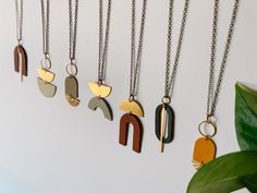 five different types of necklaces hanging on a white wall next to a potted plant