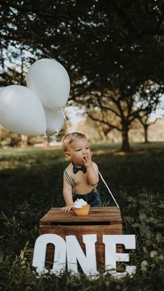 a young boy sitting on top of a wooden box with some balloons in the air