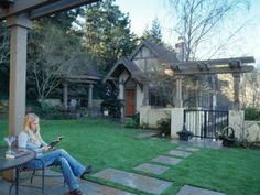 a woman sitting at a table on her cell phone in front of a house with a yard