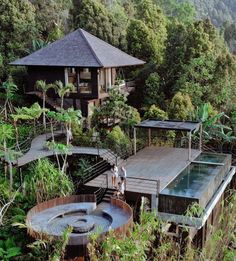 two people standing on the deck of a wooden house surrounded by trees and greenery