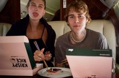 two people sitting at a table with plates and boxes in front of them, making funny faces