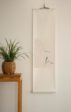 a plant sitting on top of a wooden table next to a wall mounted art piece