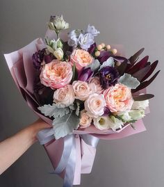 a person holding a bouquet of flowers with purple and pink blooms on it's side