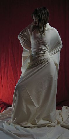 a woman in a white dress standing on a bed with her hands behind her head