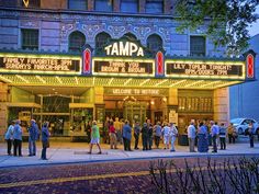 a group of people standing in front of a theater marquee with lights on