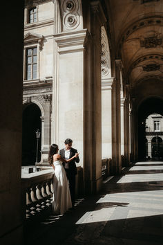 a bride and groom standing next to each other in front of a building with columns