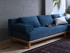 a blue couch sitting on top of a wooden floor next to a rug and window