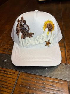 All white trucker hat, howdy, horse, sunflower and star patches on it. White Patches Hat For Summer, Country Style White Baseball Cap, Trendy White Hat For Country Events, White Western Style Snapback Hat, Western Style White Trucker Hat With Curved Brim, White Western Style Snapback Baseball Cap, Country Style White Snapback Hat, White Flat Brim Baseball Cap For Rodeo, Adjustable White Baseball Cap With Patches