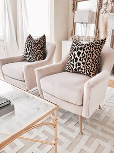 two white chairs with leopard print pillows on them in front of a mirror and fireplace