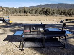 an outdoor grill is set up in the middle of a field with a tractor behind it