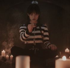 a woman sitting on the ground in front of candles with one hand up to her mouth