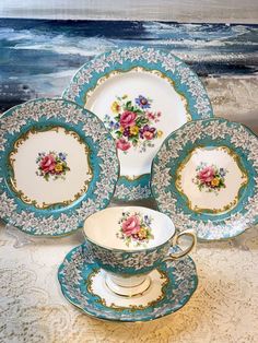 four tea cups and saucers on a table with an ocean scene in the background