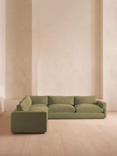 a large green couch sitting on top of a wooden floor next to a white wall