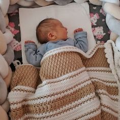 a baby laying in a crocheted blanket next to stuffed animals and blankets on the floor