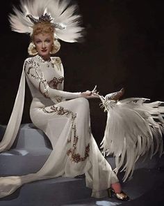 a woman in white dress sitting on steps with large feathers around her head and arms