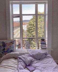 an unmade bed sitting in front of a window next to a book shelf filled with books