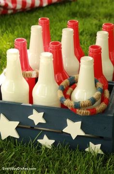 a wooden crate filled with red, white and blue bottles on top of green grass