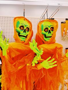 two people dressed in orange and green costumes with hands out to the side, one wearing a skeleton mask