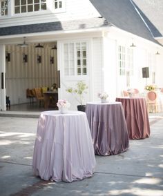 two round tables covered with pink and purple tablecloths in front of a white house